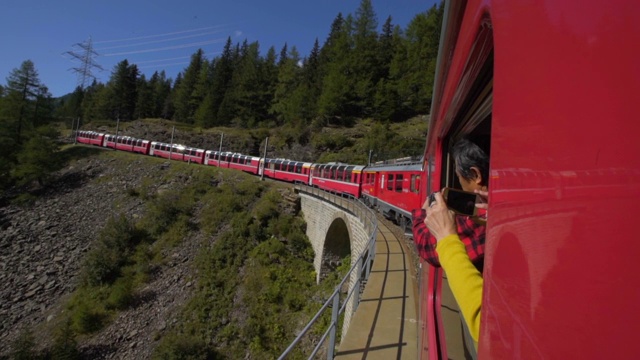 游客通过窗户拍摄火车在森林中的曲线和桥上移动的手机视频——瑞士的阿尔卑斯山视频素材