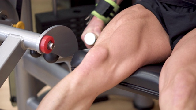 特写镜头的男子运动员与肌肉腿在健身房的腿卷曲训练。4 k。视频下载