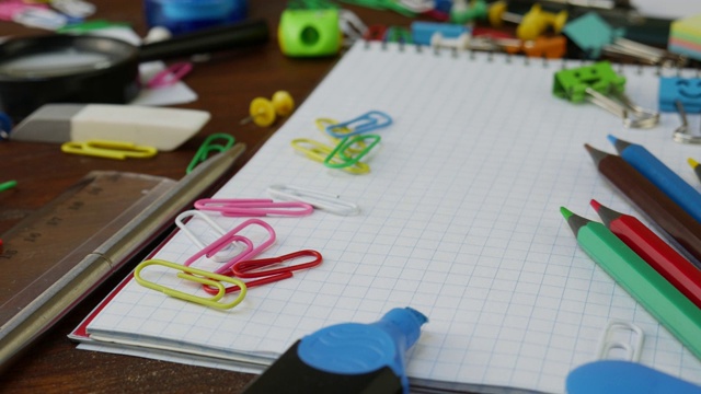 彩色铅笔，回形针和笔记本在棕色木制的书桌上视频素材