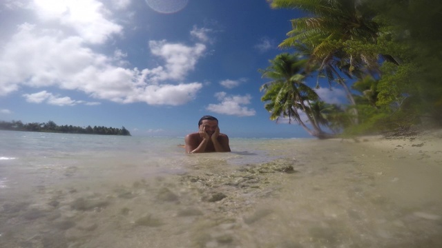 沙滩上有鹅卵石(珊瑚)有椰子树，人躺在海里视频下载