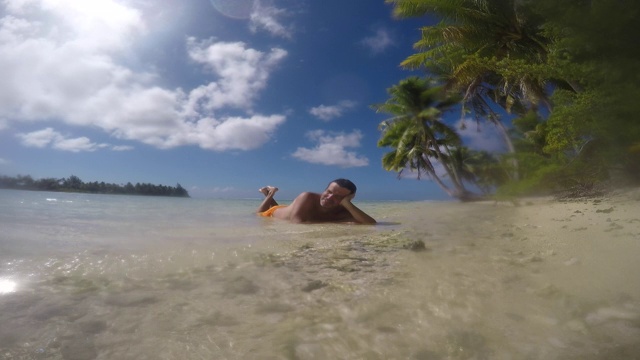 海滩上有鹅卵石(珊瑚)和椰子树，人躺在海里视频下载