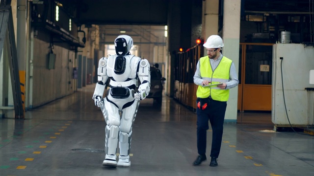 一个工程师和一个机器人正沿着工厂走视频素材