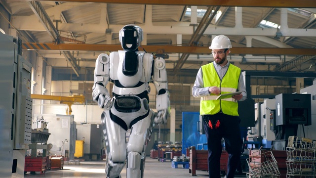 机器人在一名男性专家的控制下沿着工厂行走视频素材