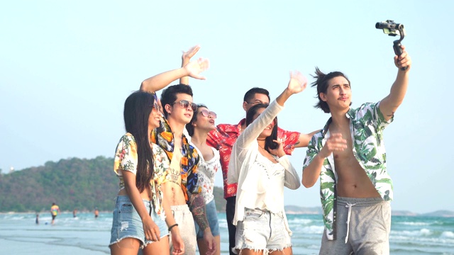 低角度正面镜头:日落时分，6个快乐的朋友在海滩上用智能手机自拍视频素材