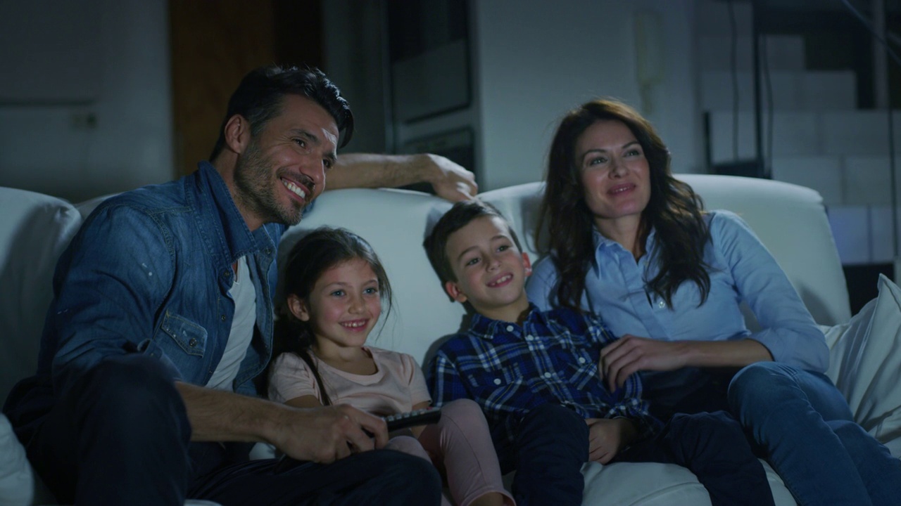 晚上在客厅沙发上看电视的幸福家庭的慢镜头。视频下载