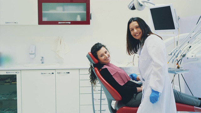 病人正坐在牙科椅上。在此期间，医生与她交流，他们一起微笑。治疗是在牙科诊所进行的。戴着医用蓝手套视频素材