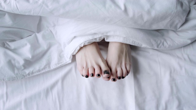 年轻女子的脚在白色毯子下面。保健概念。早上好，在酒店房间。视频素材