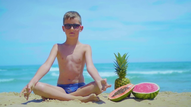 一个男孩坐在海边，在大海的背景下，旁边是奇异的水果视频下载