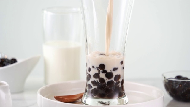 慢动作-将奶茶倒入玻璃杯中，配以台湾流行的珍珠奶茶泡，放在明亮的大理石桌上和白色的托盘上。4 k视频拍摄。视频素材