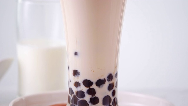 慢动作-将奶茶倒入玻璃杯中，配以台湾流行的珍珠奶茶泡，放在明亮的大理石桌上和白色的托盘上。4 k视频拍摄。视频素材