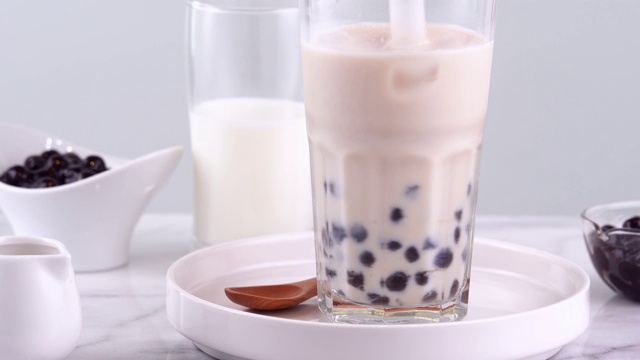 搅拌可口的台湾流行饮料木薯珍珠泡奶茶在玻璃杯上明亮的大理石桌子白色托盘，自制的概念。4 k拍摄视频视频素材