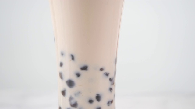 搅拌可口的台湾流行饮料木薯珍珠泡奶茶在玻璃杯上明亮的大理石桌子白色托盘，自制的概念。4 k拍摄视频视频素材