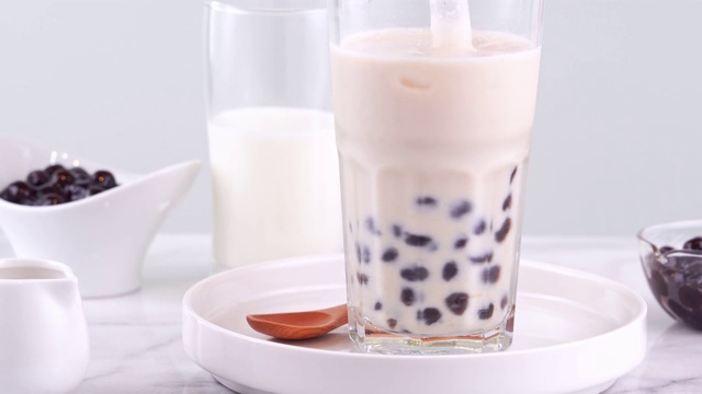 搅拌可口的台湾流行饮料木薯珍珠泡奶茶在玻璃杯上明亮的大理石桌子白色托盘，自制的概念。4 k拍摄视频视频下载