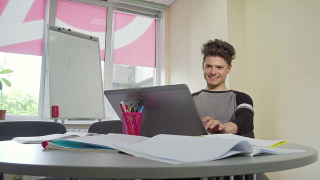 年轻的男大学生微笑着，在他的笔记本电脑上打字视频下载