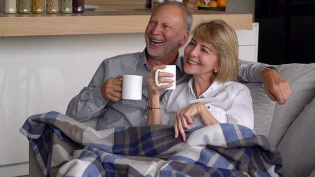 老夫妇享受着咖啡依偎在沙发上看电视聊天和微笑视频下载