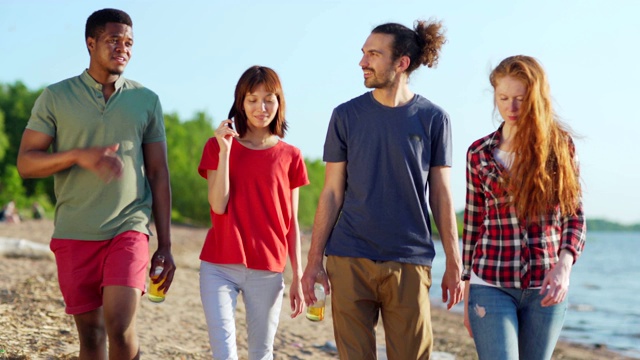 在夏日的海滩上，四个不同的年轻朋友一起散步聊天。拿着啤酒瓶的男人视频下载