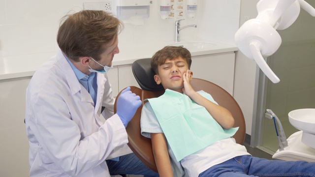 小男孩有牙痛，在牙科检查时坐在牙科椅上视频素材