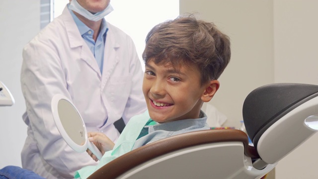 小男孩对着镜头微笑，他对着镜子检查了自己健康的牙齿视频素材