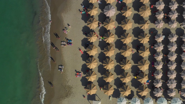 棕色沙滩伞到白色沙滩伞在右边和水在左边向下无人机镜头视频素材