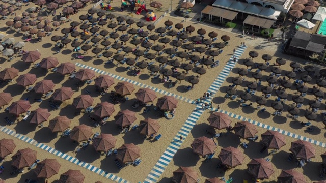 在意大利海滩上充满了人们在阳光下放松的棕色沙滩伞和条纹人行道的角度航拍视频素材