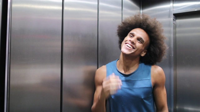 一个非洲年轻人在电梯镜子前摆弄头发，门开了，走了出来视频素材