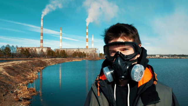 一个年轻男子的肖像在呼吸器或防毒面具。背景中，烟雾来自一个水电站的管道。视频素材