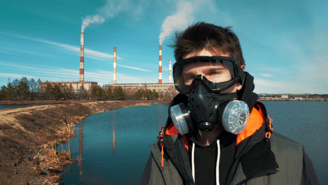 一个年轻男子的肖像在呼吸器或防毒面具。背景中，烟雾来自一个水电站的管道。视频素材