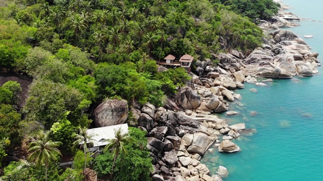 热带岛屿上的小房子。阳光明媚的泰国，苏梅岛海岸上的小平房，靠近平静的海面。火山岩石和悬崖无人机俯视图。视频下载