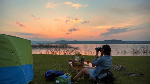 暑期两个亚洲背包客在湖边欣赏日落的慢镜头。他们是快乐的，有乐趣的假期，放松的时刻。青少年自然户外日常生活的概念视频素材