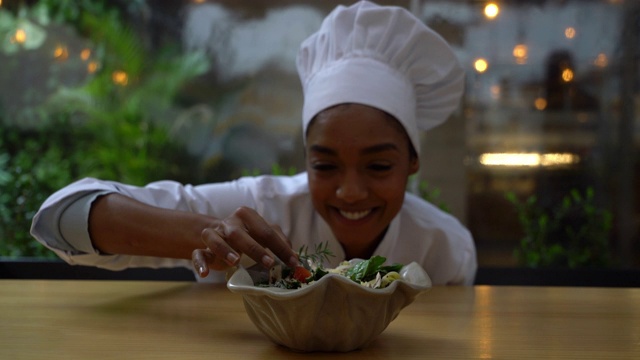 美丽的黑人女厨师在面对镜头微笑的同时为沙拉做最后的润色视频素材