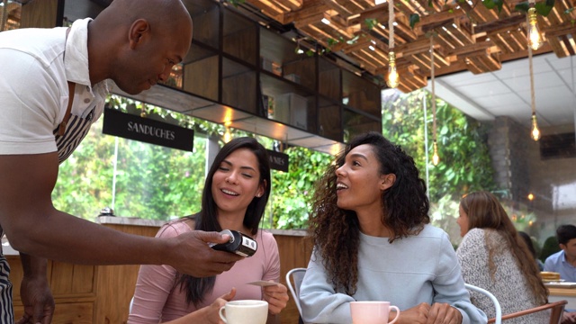 漂亮的女性朋友们一边喝着咖啡，一边用信用卡给友好的服务员结账视频下载