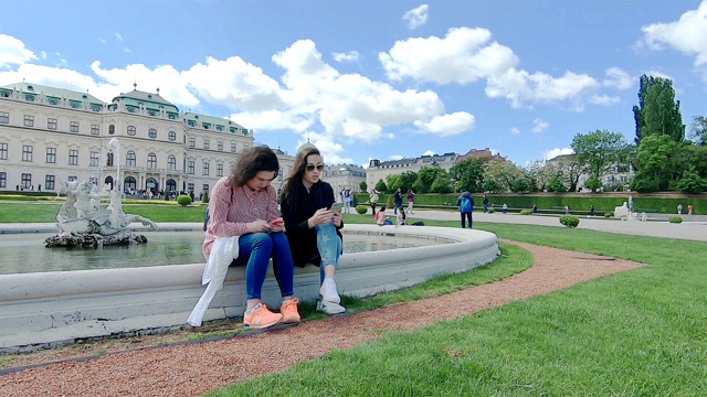 游客们坐在喷泉附近，通过智能手机阅读这座宫殿的历史。视频素材