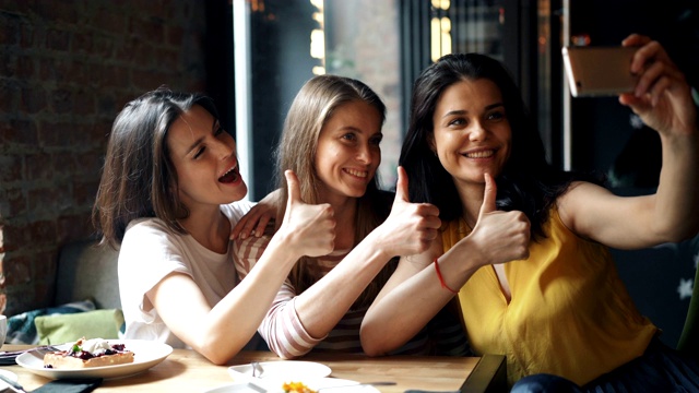 快乐的年轻姑娘们在咖啡馆里竖起大拇指自拍视频素材