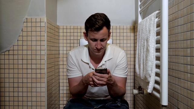 男人在厕所里用智能手机。视频下载