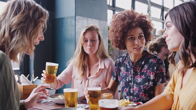 一群年轻的女性朋友在餐厅酒吧用啤酒敬酒-用慢镜头拍摄视频素材