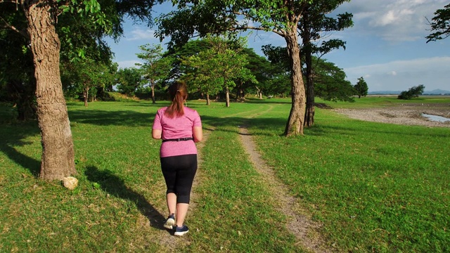 亚洲妇女慢跑在傍晚的阳光与树木的自然。健身和健康生活理念。后视图的女孩在运动服跑步锻炼。慢动作视频素材