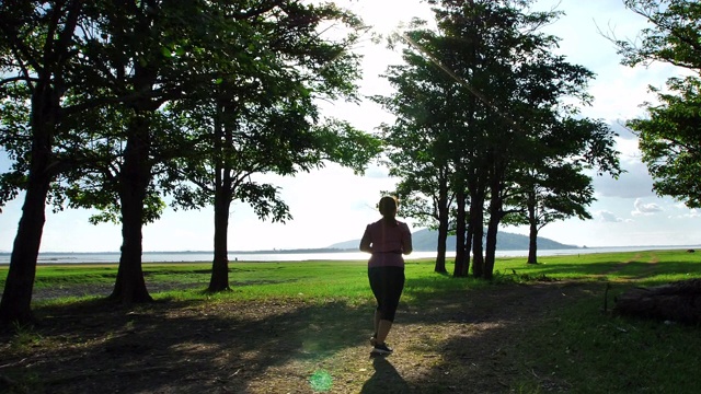 亚洲女性在傍晚的阳光下在大自然中慢跑。健身和健康生活理念。后视图的女性在运动服跑步锻炼。慢动作视频素材