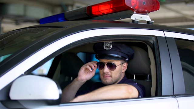 年轻的警察戴着太阳镜在车里，对着镜头微笑，重要的工作视频下载