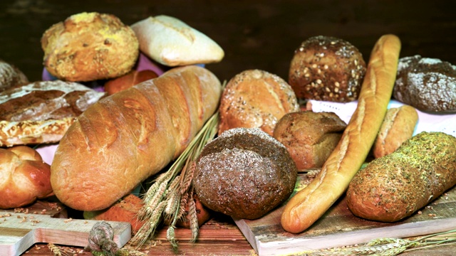 各种各样的新鲜面包和小麦在黑暗的木制背景。白面包的特写镜头。视频下载