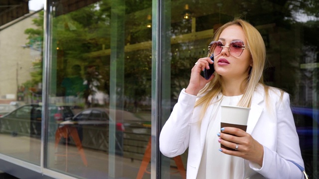 漂亮的金发女人拿着咖啡杯在街上打电话视频素材