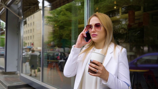 年轻时髦的金发女人拿着咖啡杯在街上打电话视频素材