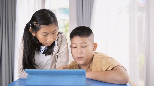 快乐的亚洲男孩和女孩在家里使用平板电脑。视频下载