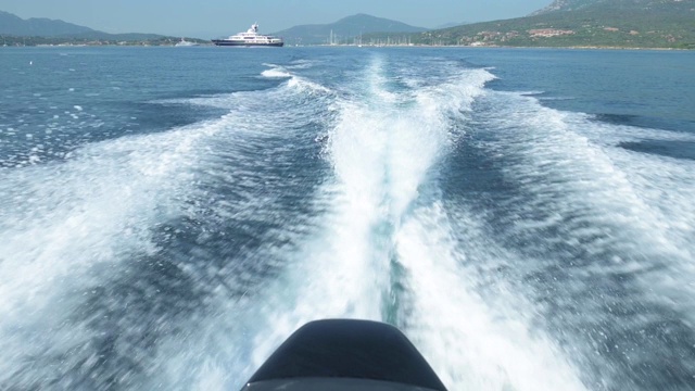 一艘充气船在美丽的蓝色海面上航行留下的水迹的慢动作视频，撒丁岛，意大利。视频下载