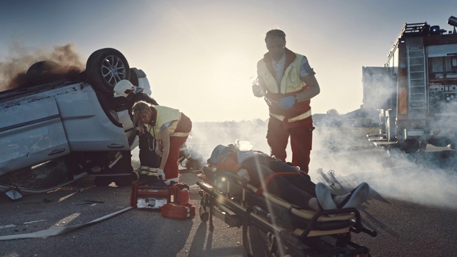 在车祸交通事故现场:医护人员给事故中的女性受害者提供急救氧气面罩。消防队员灭火并使用液压切割器救出其他乘客视频素材