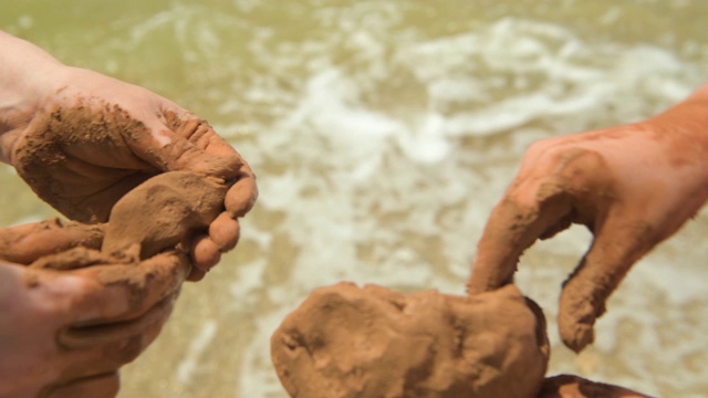 手在海滩上制作粘土的特写，沙子和波浪作为背景，夏天和旅游的概念。视频下载