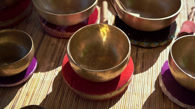 一名亚洲神药女大师表演藏式碗疗愈仪式的超慢镜头。用西藏唱碗冥想。她坐在凉亭里冥想，背景是美丽的瀑布视频素材