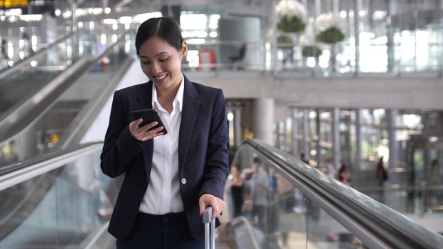 亚洲女商人在机场候机楼的自动扶梯上使用电话视频素材