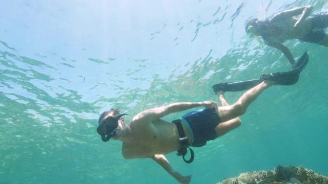 年轻的男人和女人戴着浮潜面具在蓝色的大海里游泳，水下风景。男人和女人一起浮潜在透明的海在阳光水槽的水。视频素材