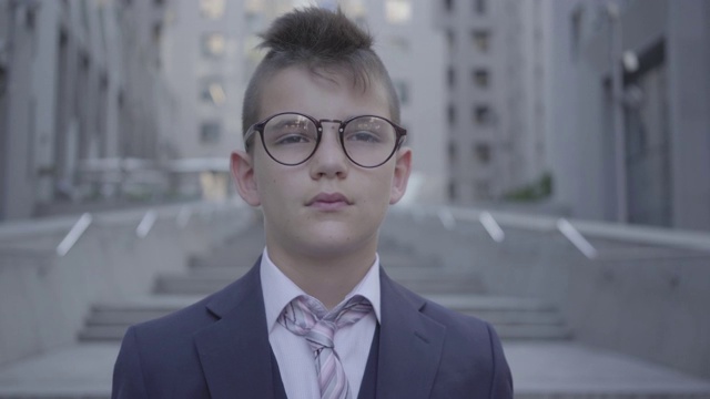 肖像英俊的穿着整齐的男孩戴着眼镜站在街上看着相机。视频下载