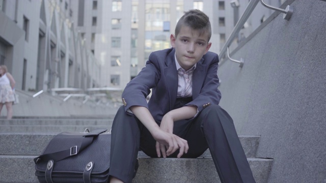 坐在街上楼梯上的一个穿着考究的可爱男孩。视频下载